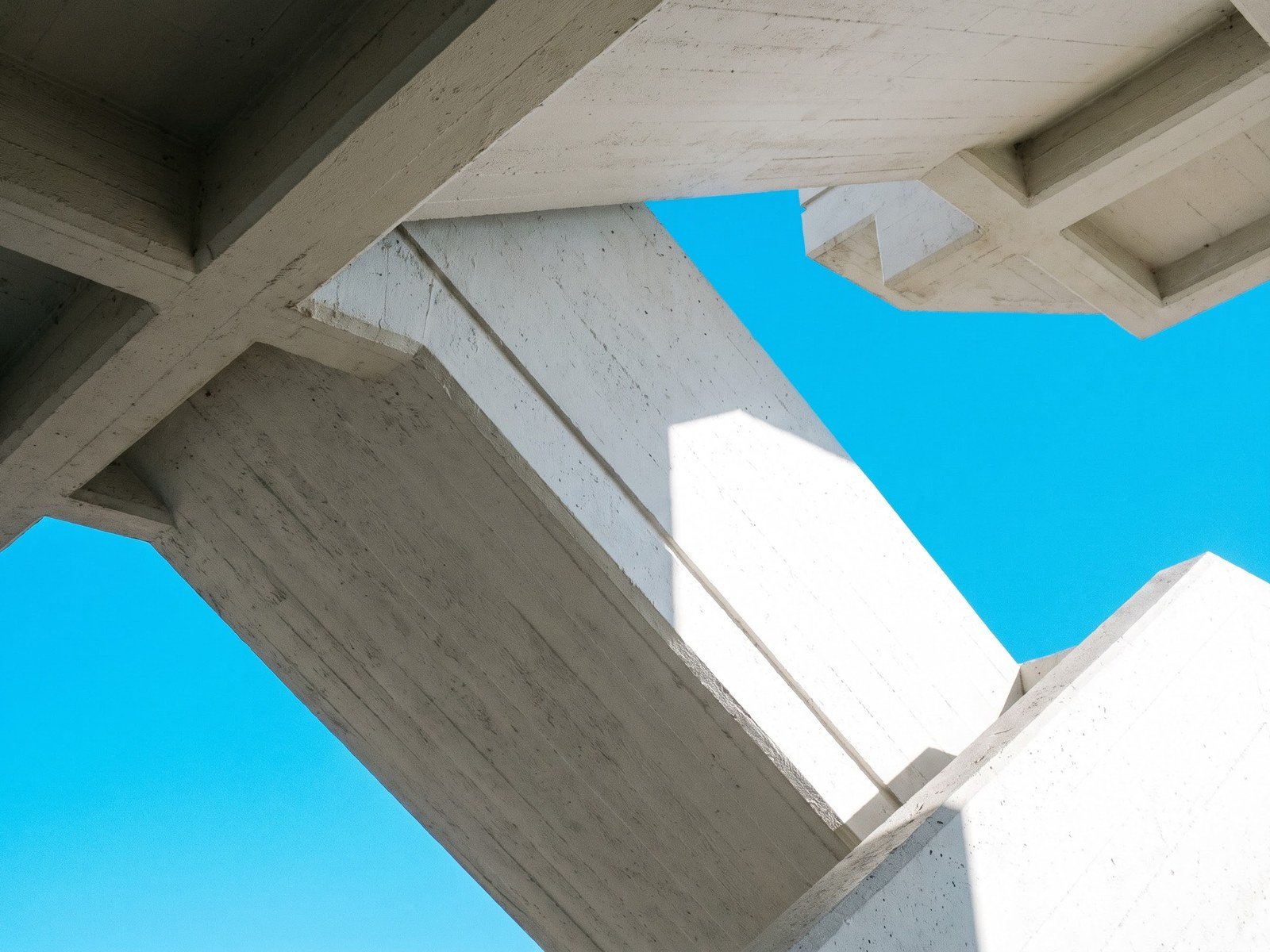 Looking up at intersecting white concrete beams against a vivid cyan sky