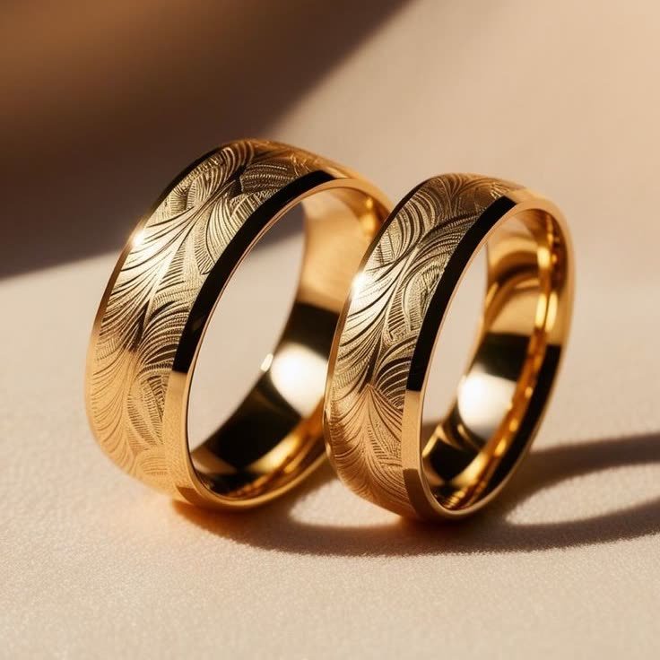 Pair of engraved gold wedding bands in warm light on a cream ground