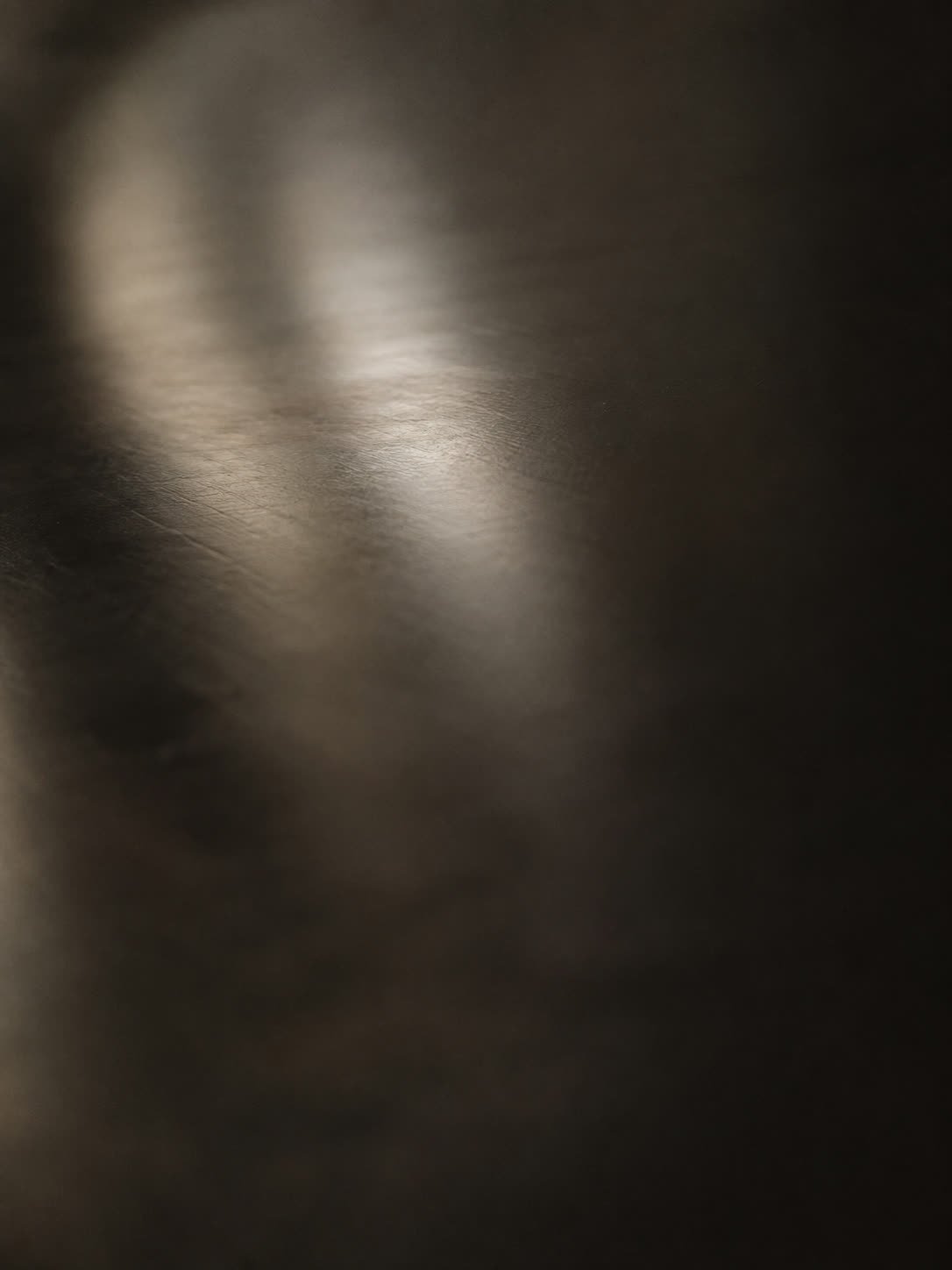 A dark polished surface with a soft highlight sweeping across it, near-abstract
