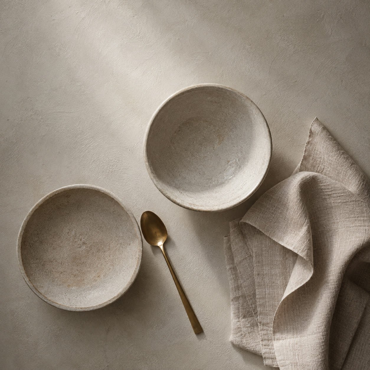 Overhead still life — two stone bowls, a brass spoon and a folded linen cloth